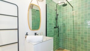 A bathroom with a white sink, a mirror, and a shower with green tiles. - Bungalow (Saint Paul)