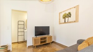 A living room with a grey sofa, a wooden TV stand, a flat-screen TV, a woven basket, and a framed picture on the wall. - Bungalow (Saint Paul)