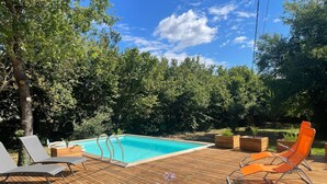 A wooden deck with a swimming pool, surrounded by trees and equipped with lounge chairs.