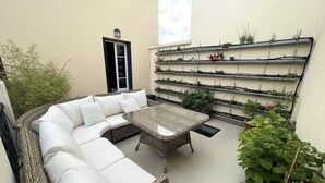 A wicker sofa with white cushions, a glass-top coffee table, and a wall-mounted plant shelf. - Pleasant town house on the outskirts of Paris (Nanterre)