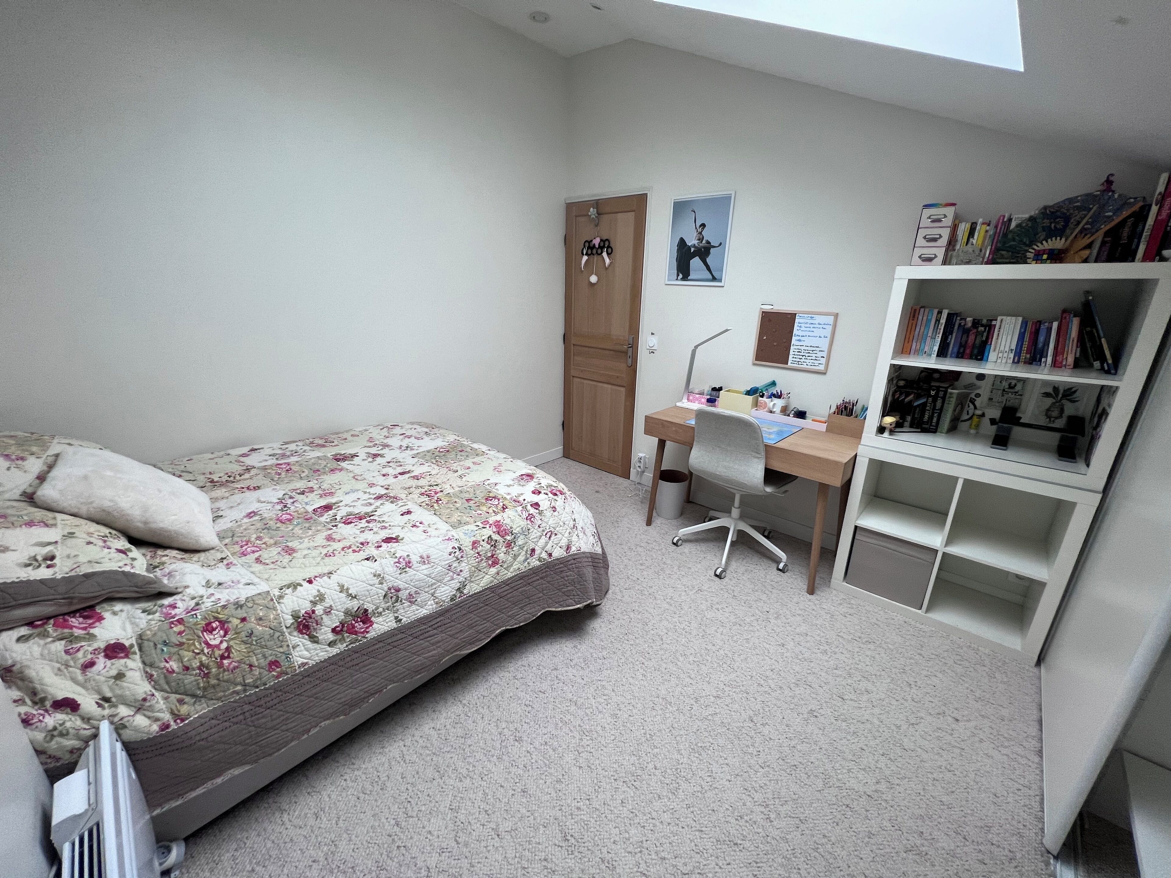 Een slaapkamer met een bed, een bureau en een boekenplank.
