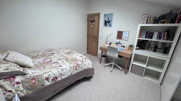 Een slaapkamer met een bed, een bureau en een boekenplank.