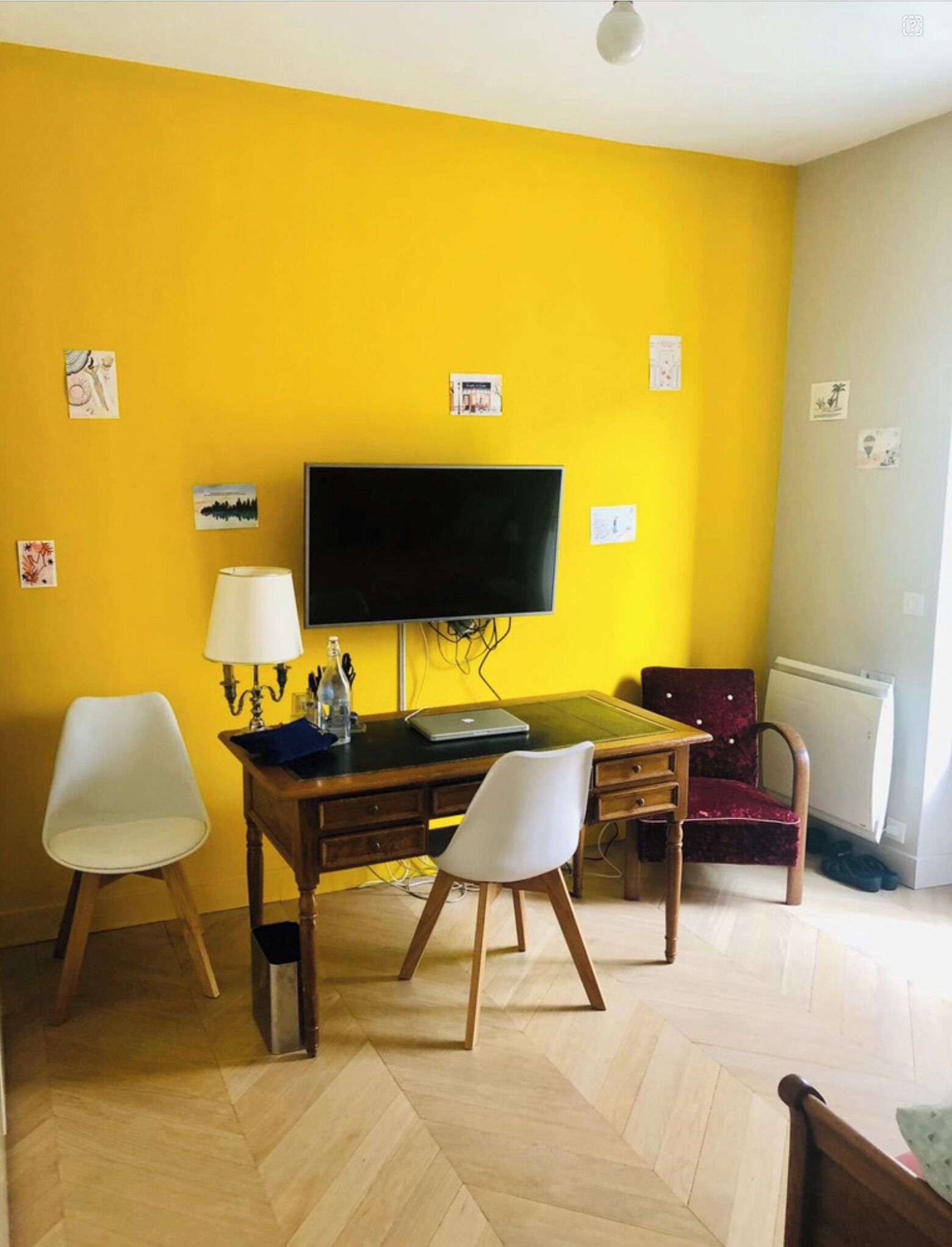 Une pièce avec un mur jaune, un téléviseur à écran plat, un bureau en bois, deux chaises blanches et une chaise rouge.
