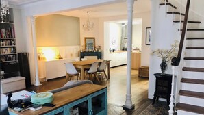 A spacious living area with a dining table, chairs, a kitchen in the background, and a staircase. - Pleasant town house on the outskirts of Paris (Nanterre)