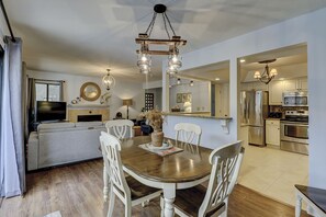 Una sala de estar moderna con una mesa de comedor, sillas blancas, una chimenea y un televisor.
