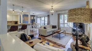 A spacious living area with a sofa, coffee table, and dining table. There is a kitchen in the background with white cabinets and a blue backsplash.