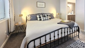 Un dormitorio con cama, lámparas de noche, mesita de noche, espejo y ventana con cortinas.
