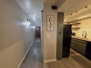 Um corredor leva a uma cozinha, com uma porta que diz 'LET'S EAT'.