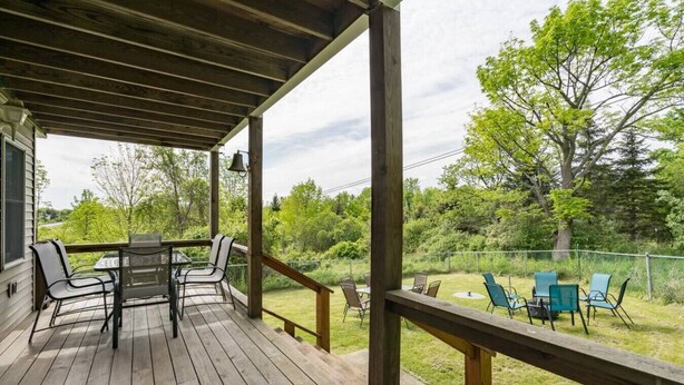 Un terrazzo in legno con tavolo e sedie, affacciato su una zona verde alberata.