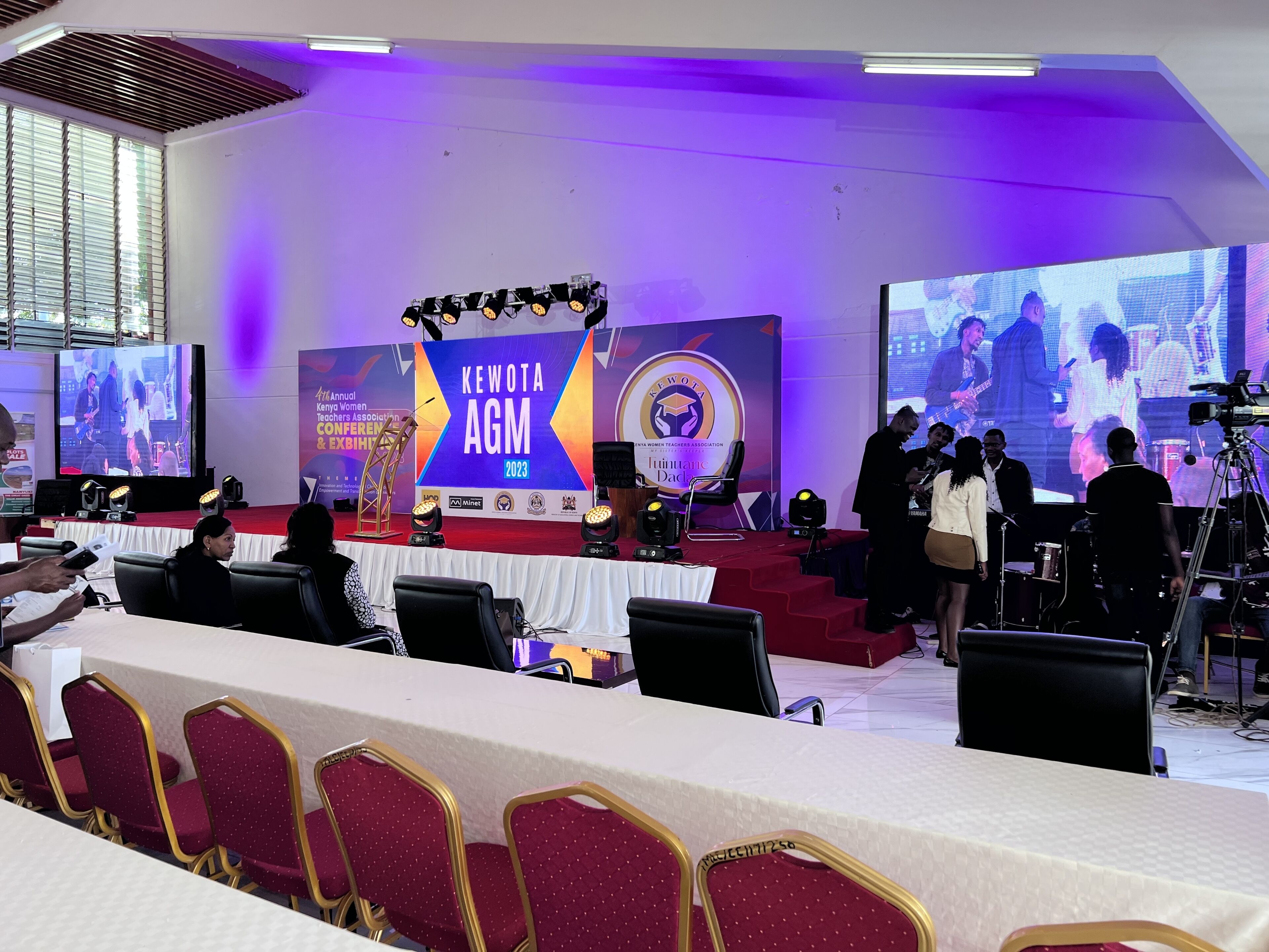 Un salón de conferencias con un escenario, sillas y una pantalla grande mostrando una presentación.