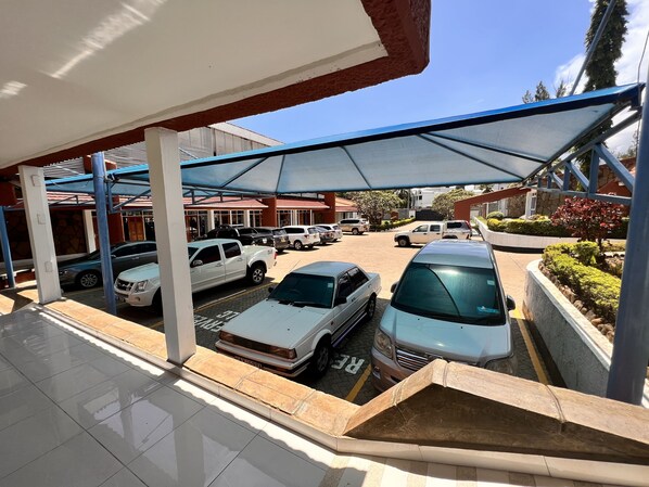 A parking area with multiple cars, a covered walkway, and a building with a red roof in the background.