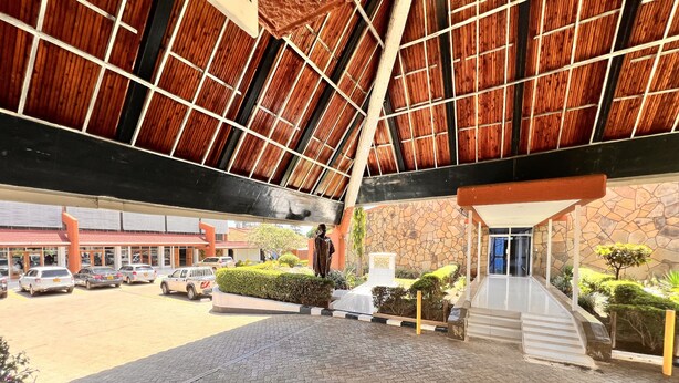 A building entrance with a stone facade, a statue, and a parking lot with cars. - Tom Mboya Labour College (Kisumu)
