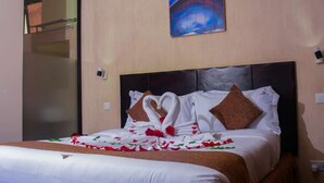 A hotel room with a neatly made bed, a painting on the wall, and a glass door leading to another room. - Tom Mboya Labour College (Kisumu)