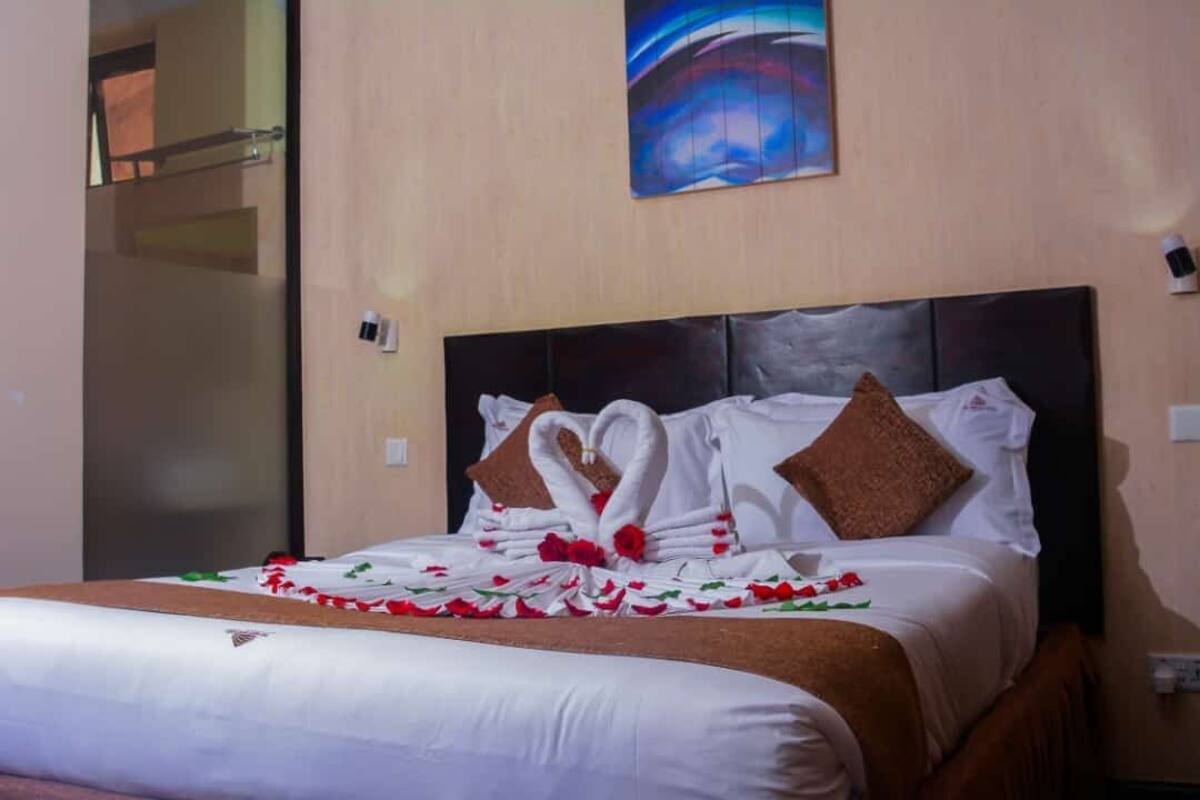 A hotel room with a neatly made bed, a painting on the wall, and a glass door leading to another room.