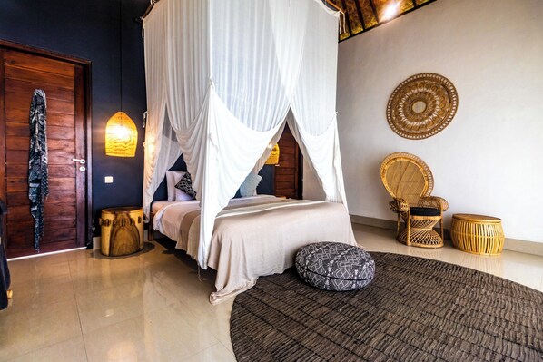 A bedroom with a four-poster bed, a wooden door, a woven chair, and a round wooden stool. - Pelangi Villas Sidemen (Sidemen)