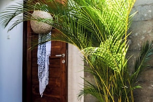 A wooden door with a patterned cloth hanging on it, surrounded by lush green foliage.