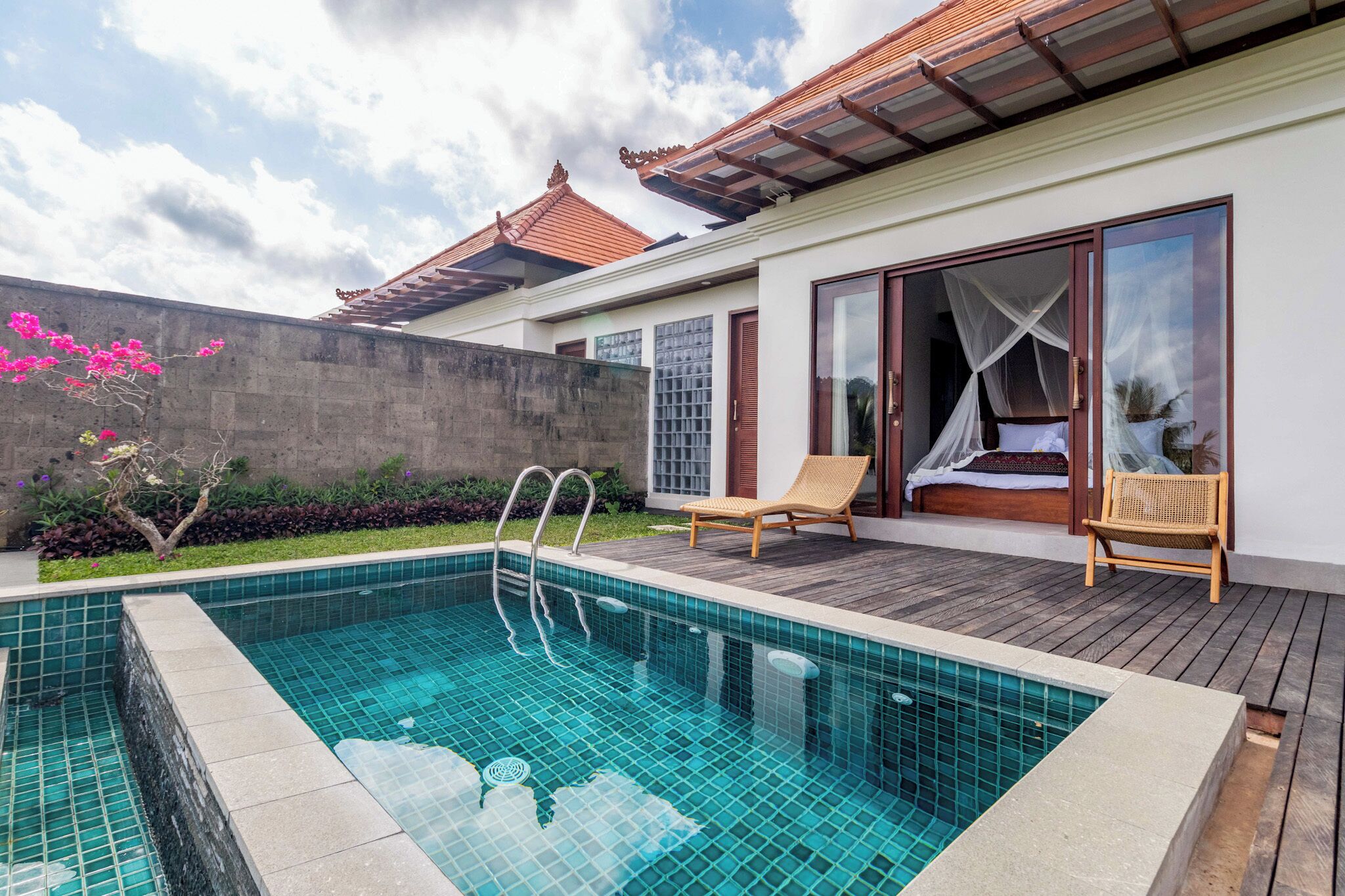A swimming pool with a wooden deck, a bed with a canopy, and a traditional tiled roof.