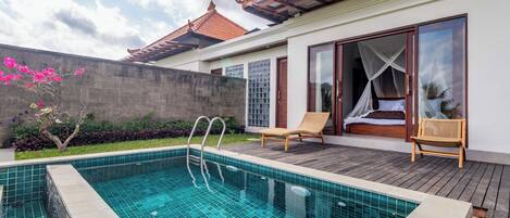 A swimming pool with a wooden deck, a bed with a canopy, and a traditional tiled roof.