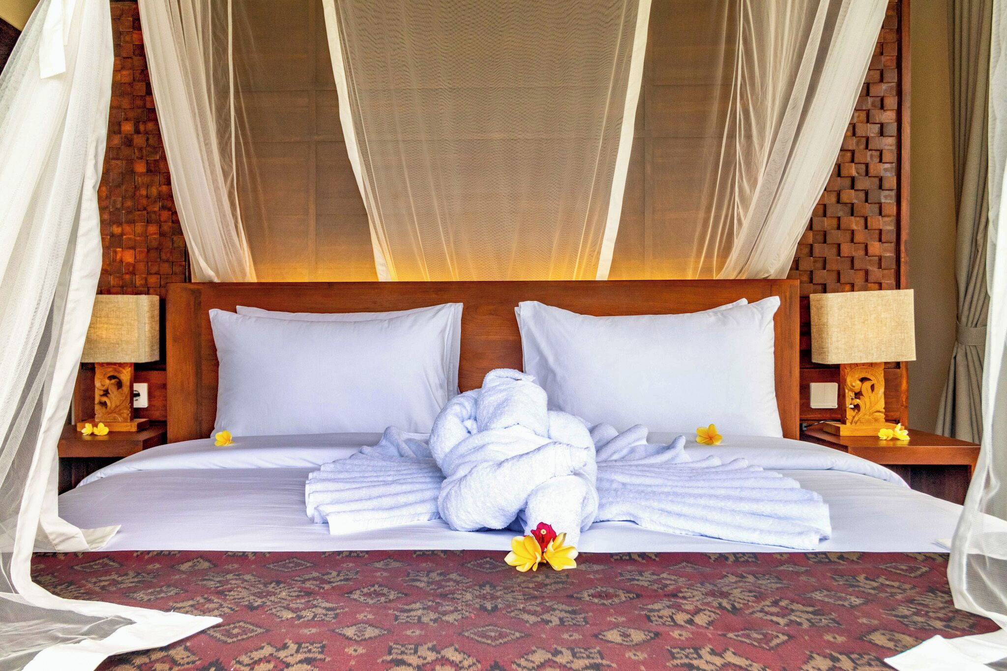 A hotel room with a bed, white linens, a wooden headboard, and a mosquito net.