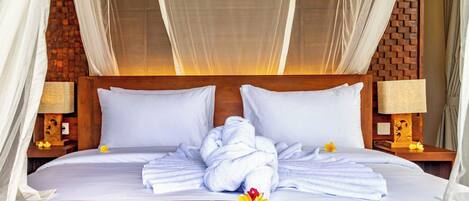 A hotel room with a bed, white linens, a wooden headboard, and a mosquito net.