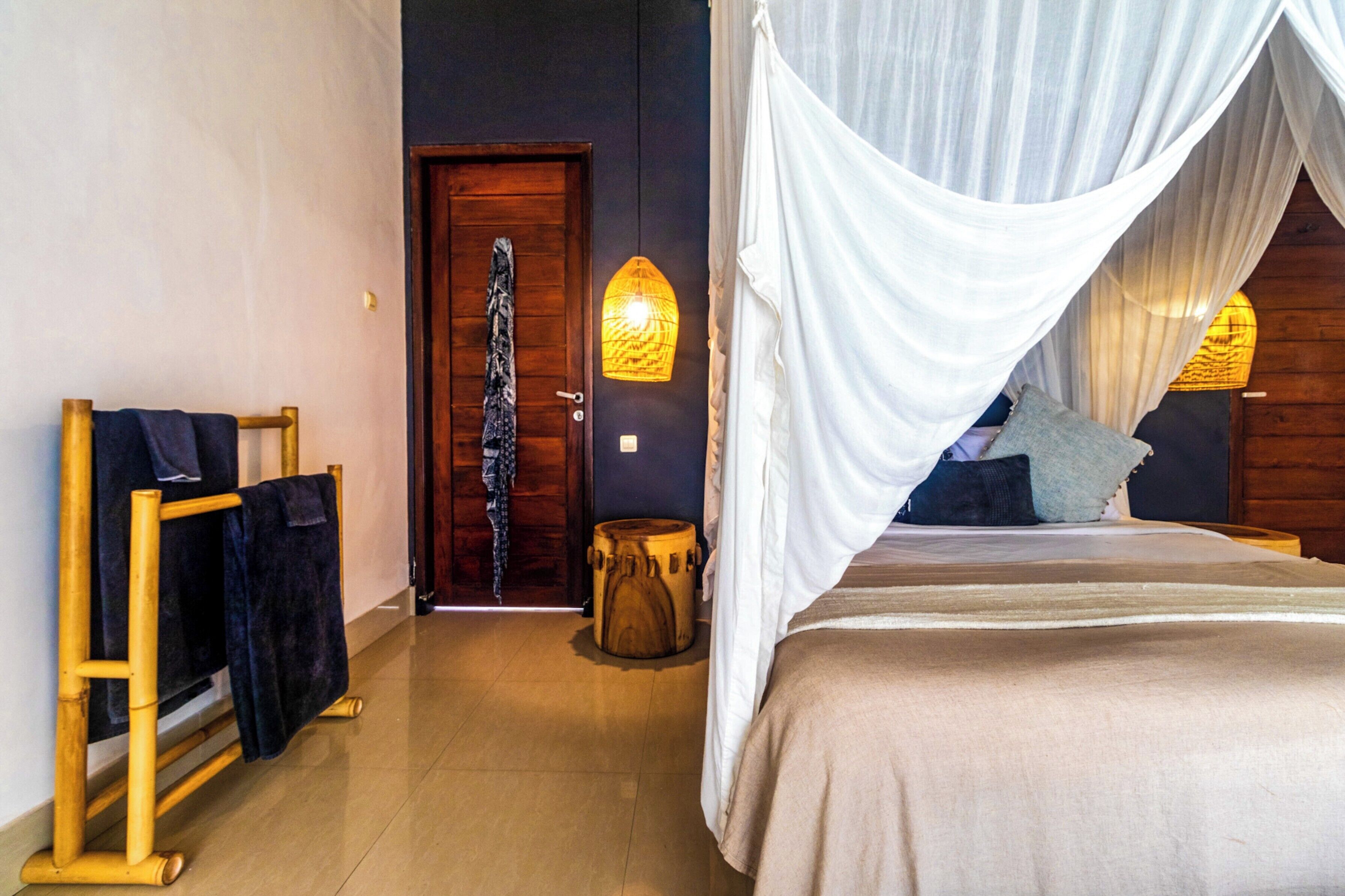 A bedroom with a bed, a wooden door, a towel rack, and a small round table.