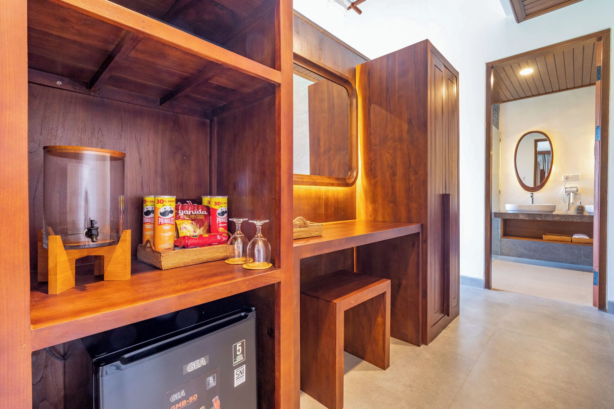 Un baño de hotel con muebles de madera, un lavamanos, un espejo y un refrigerador.