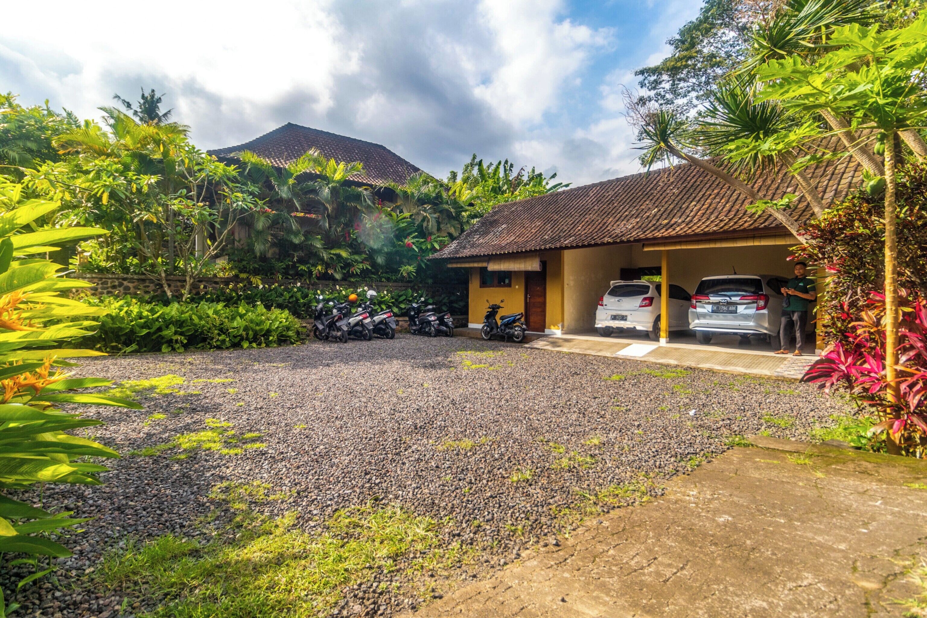 A residential area with a house, a gravel driveway, and parked vehicles.