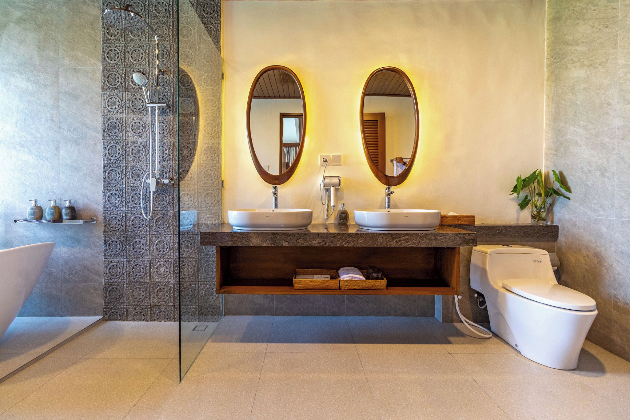 Un baño moderno con cabina de ducha de vidrio, dos lavamanos, un inodoro y un espejo grande.