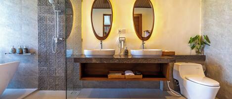Un baño moderno con cabina de ducha de vidrio, dos lavamanos, un inodoro y un espejo grande.
