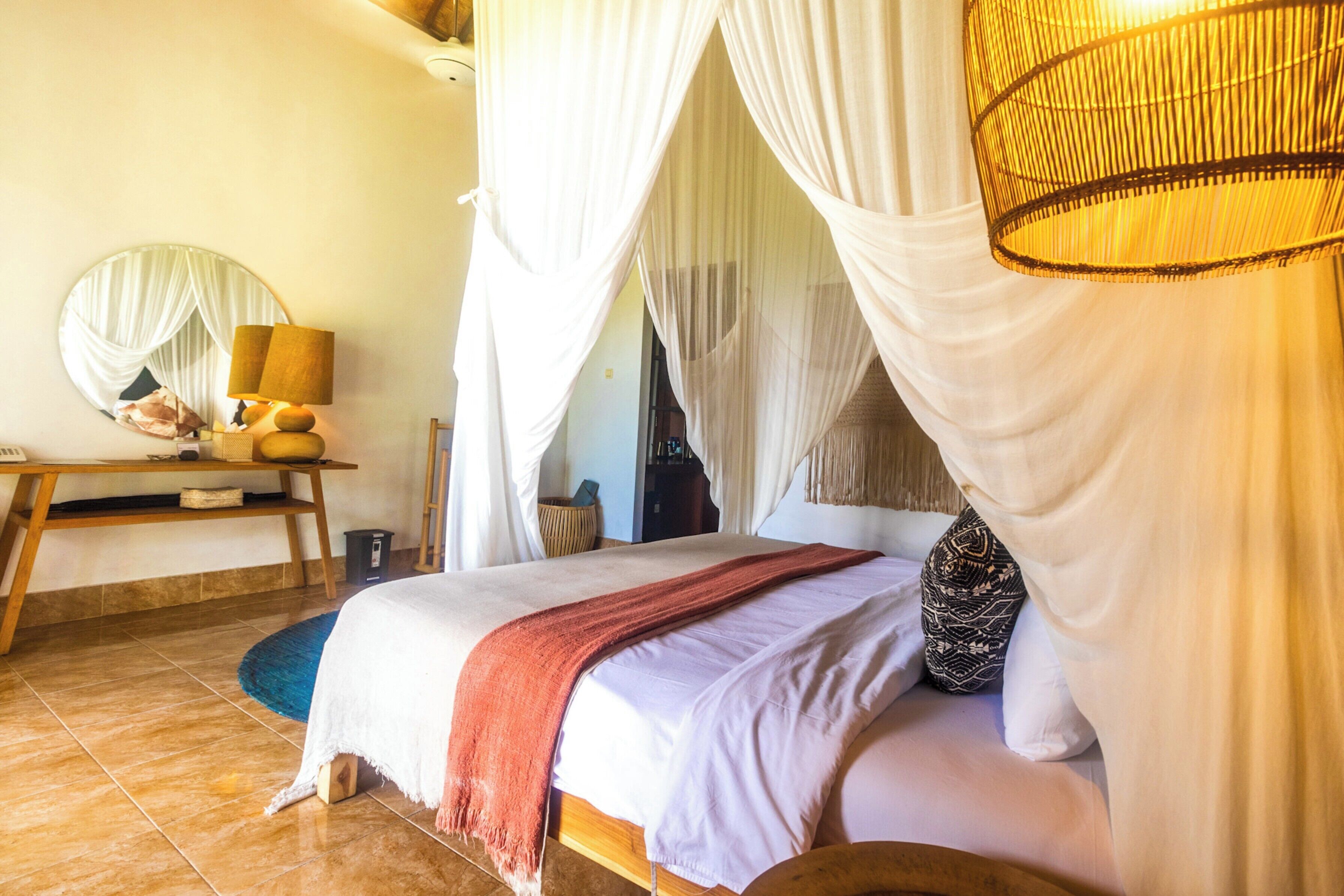 Ein Bett mit Baldachin, ein Nachttisch mit Lampe und ein Spiegel an der Wand.