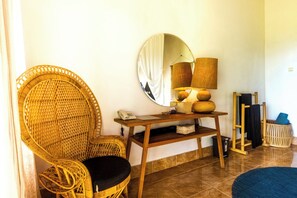 Une chaise en osier, un miroir rond, une console en bois avec des lampes et un petit panier.