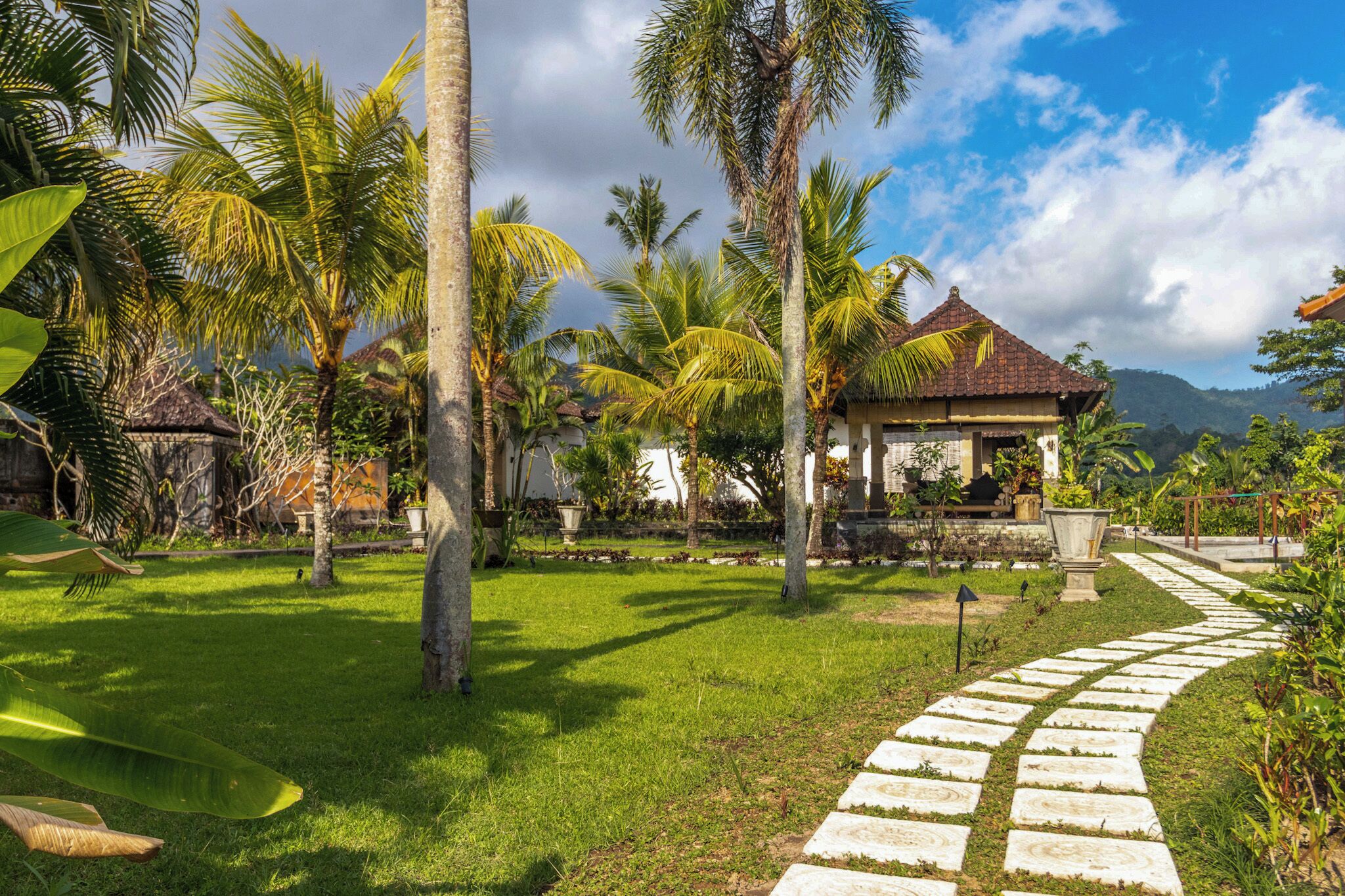 A tropical garden with a gazebo, palm trees, and a stone pathway.