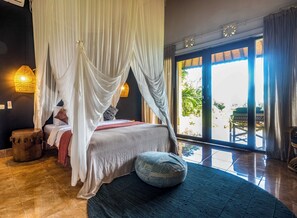 A bedroom with a canopy bed, a view of the outdoors, and a wooden stool. - Pelangi Villas Sidemen (Sidemen)