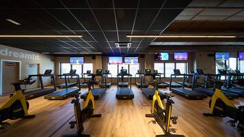 A gym with treadmills, stationary bikes, and exercise equipment. There are multiple screens displaying workout videos.