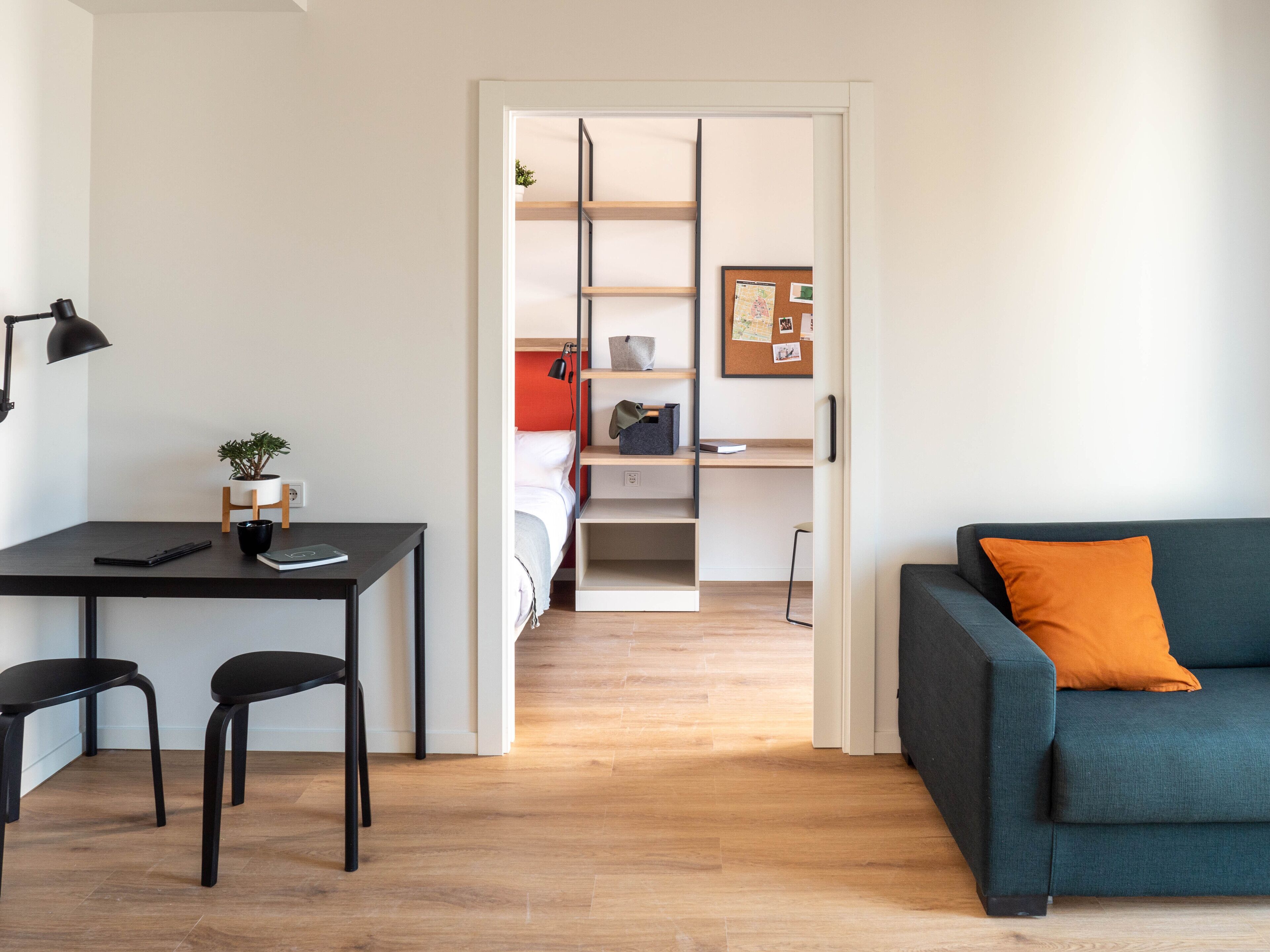 A modern, well-lit room with a desk, two chairs, a sofa, and a bed.
