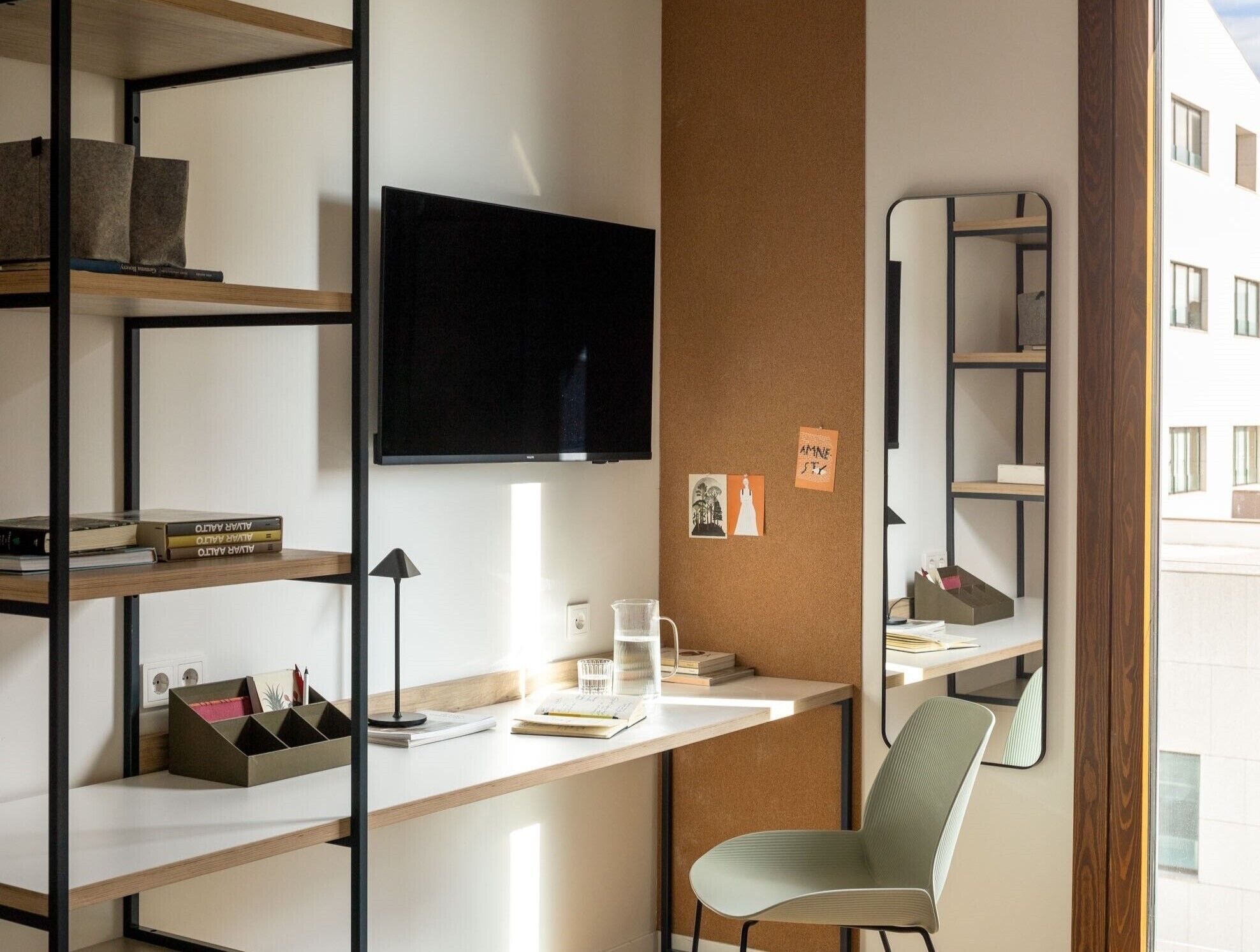 A modern office space with a desk, shelves, a chair, a TV, and a corkboard with notes.