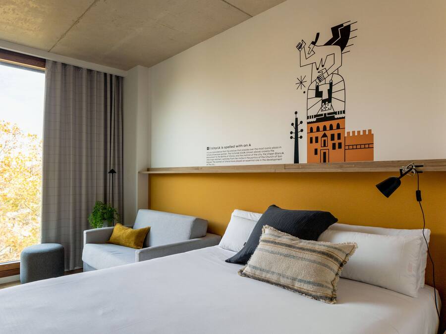 A hotel room with a bed, a sofa, a small table, and a wall with a cityscape mural.