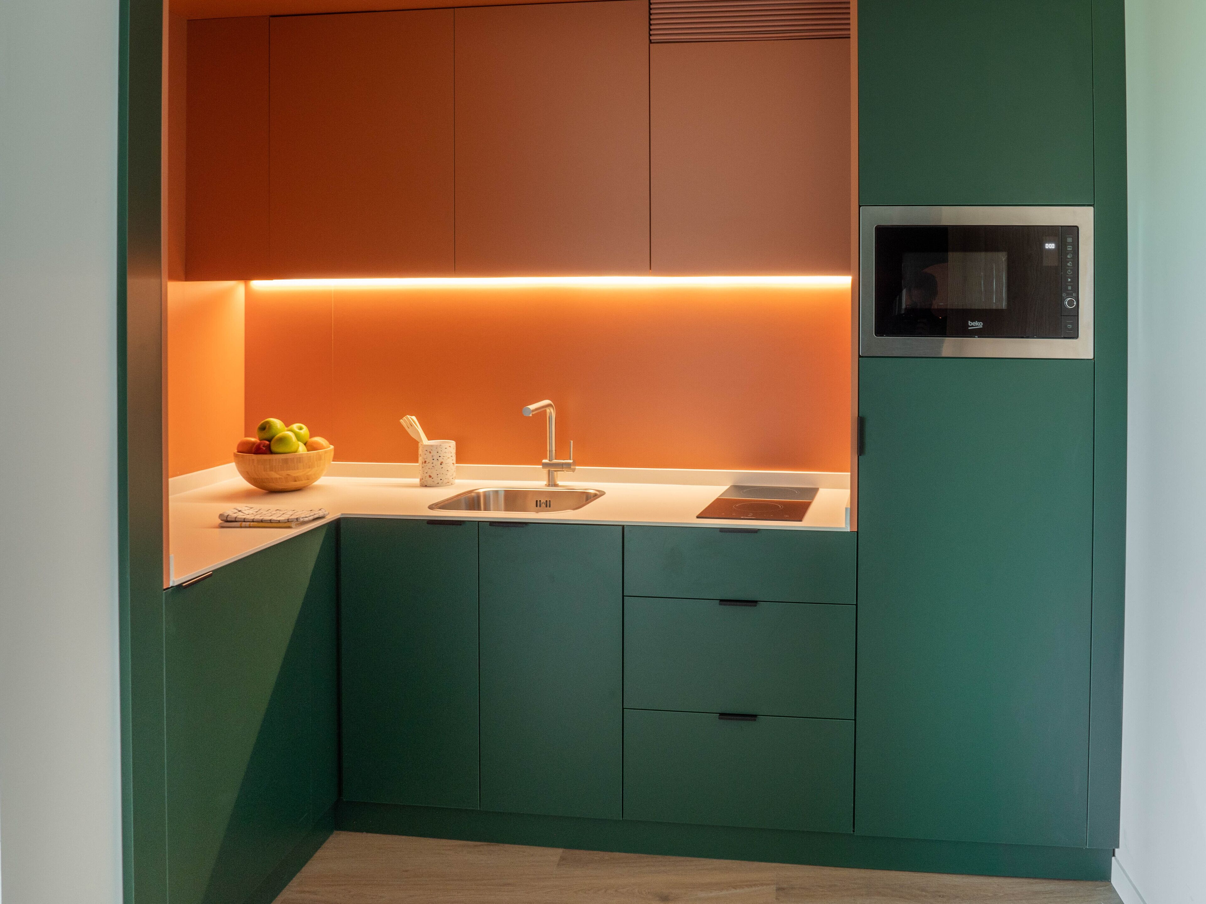 A compact kitchen with a built-in microwave, a sink, and a bowl of fruit on the counter.