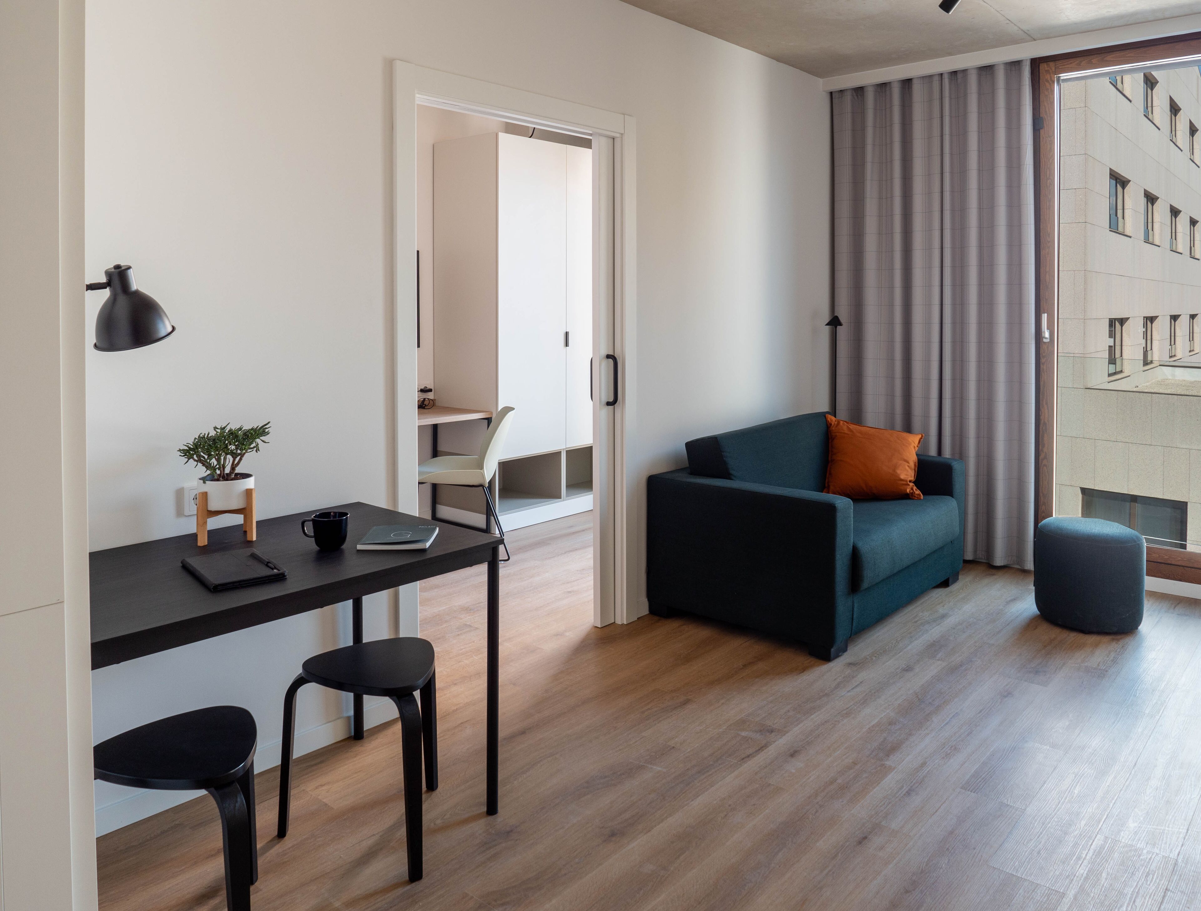 Una sala moderna con un sofá azul oscuro, una pequeña mesa con una planta y un escritorio con una silla.