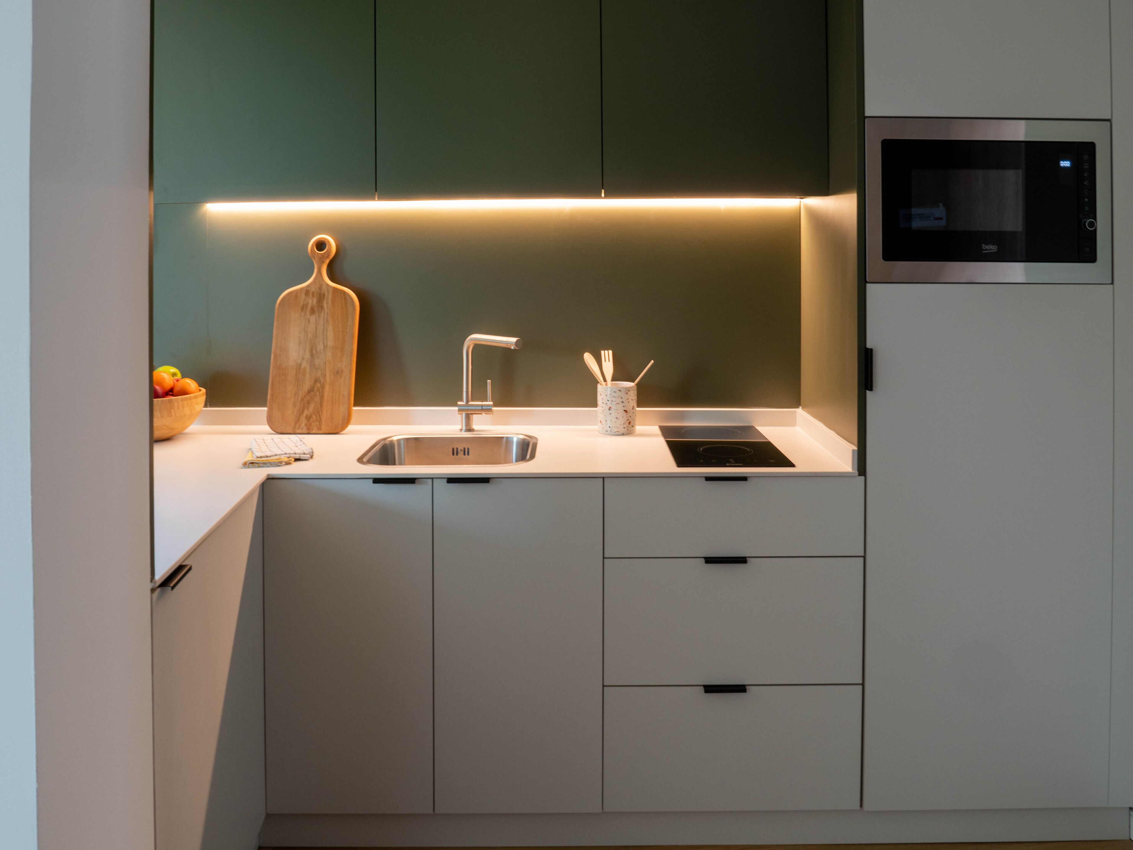 A modern kitchen with a built-in microwave, a sink, and a wooden cutting board.