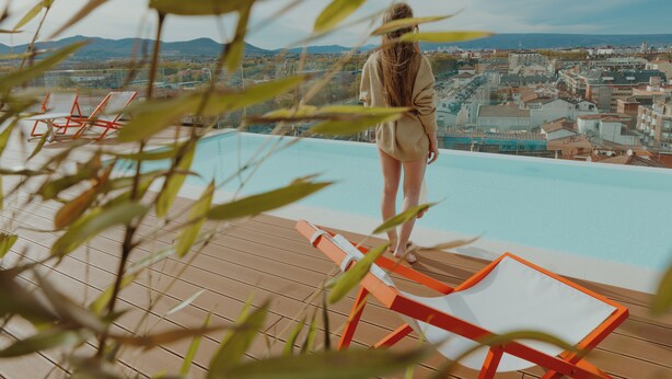 A person standing by a pool with a city view in the background. - Aparthotel Kora Green City  (Vitoria-Gasteiz)