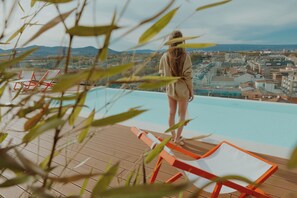 En person står vid en pool med en stadsutsikt i bakgrunden.