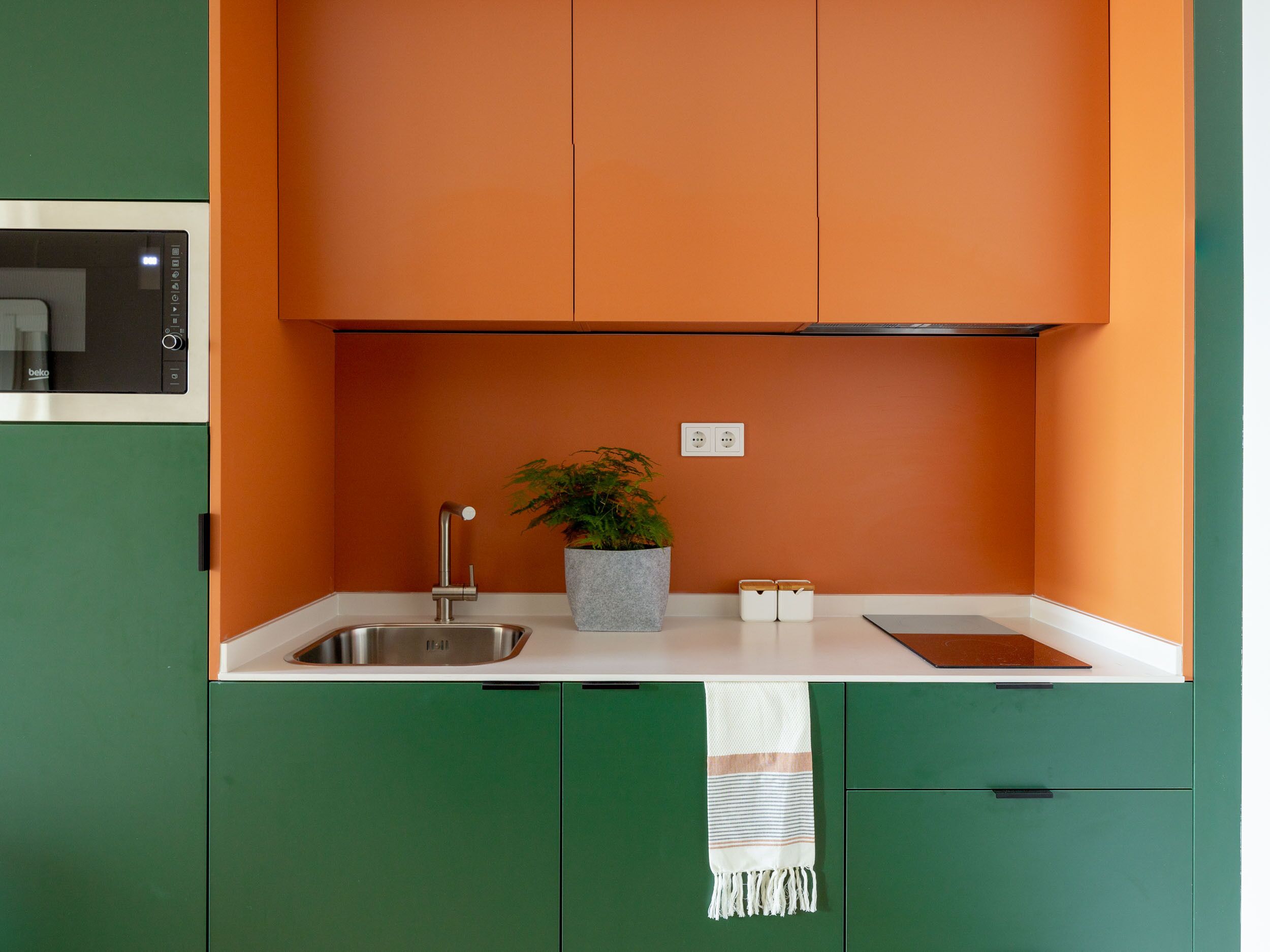 A kitchen with green cabinets, a white countertop, a sink, a stove, and a potted plant.
