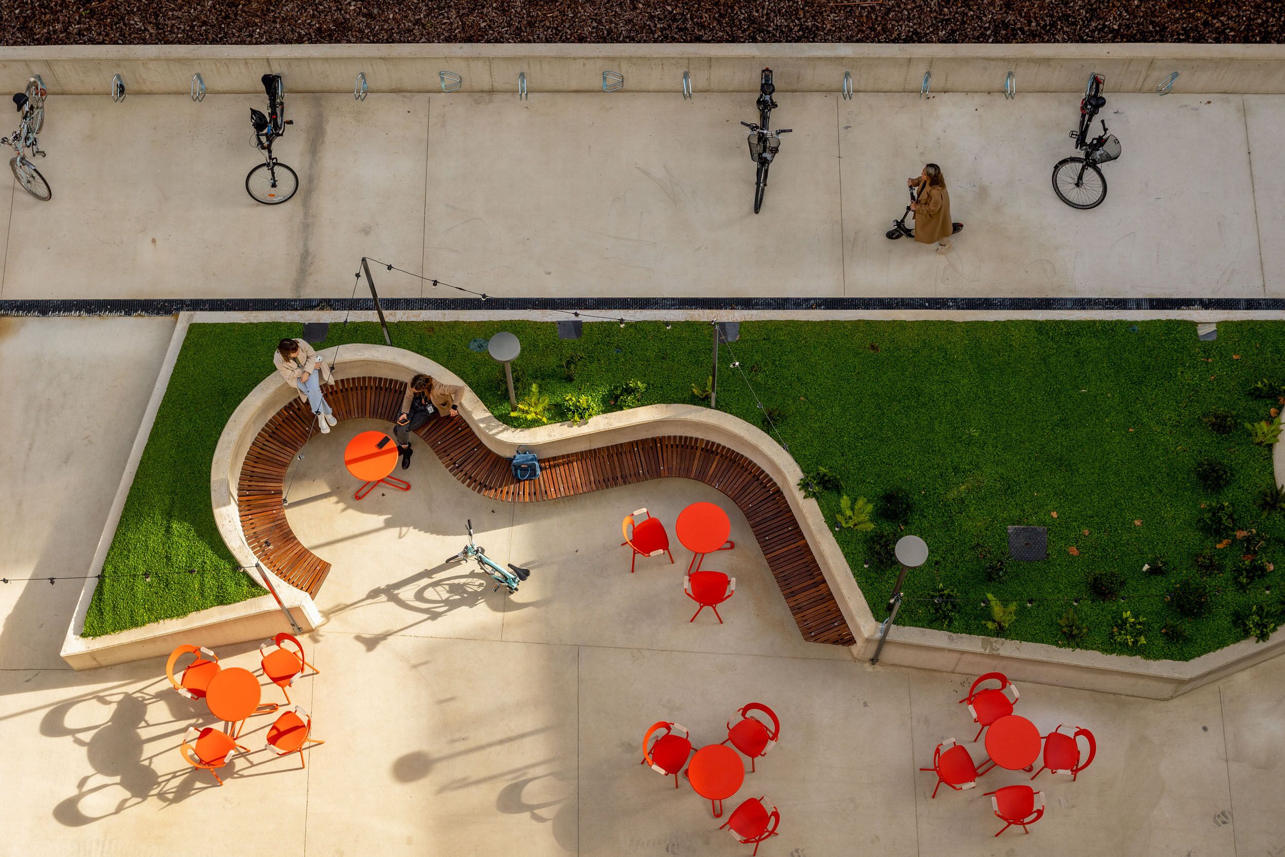Un área de patio al aire libre con un conjunto de asientos curvos, un pequeño jardín y varias bicicletas estacionadas junto a una pared.