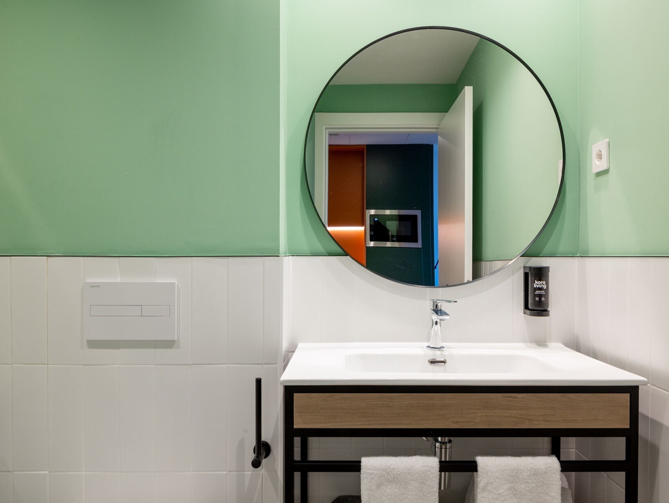 Een badkamer met een wit wastafel, een ronde spiegel en een handdoekhouder.