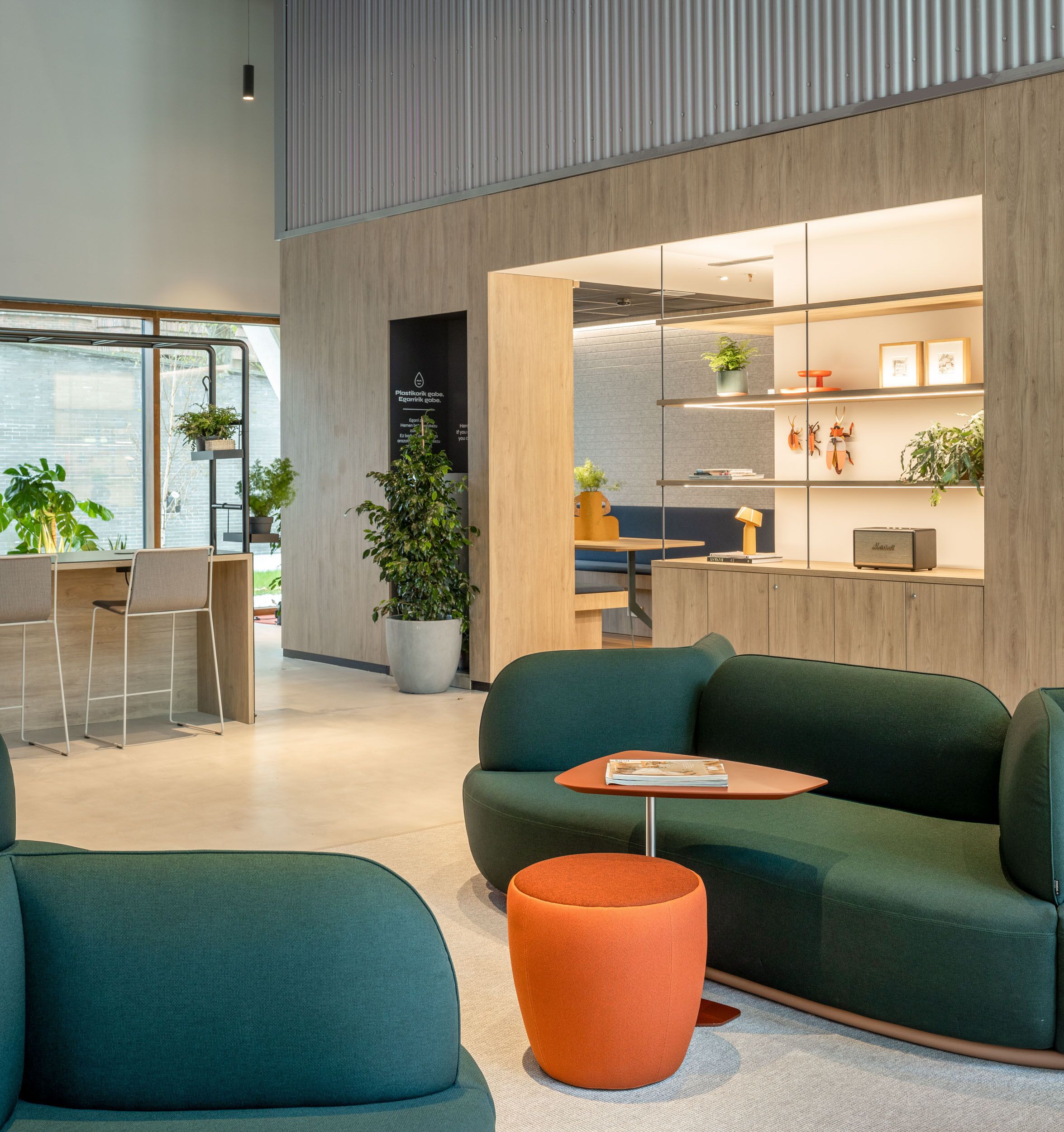A modern interior with a green sofa, orange ottoman, and a wooden desk area with chairs.