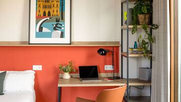 Une chambre moderne avec un bureau en bois, un ordinateur portable, une chaise, un lit et une bibliothèque agrémentée de plantes.