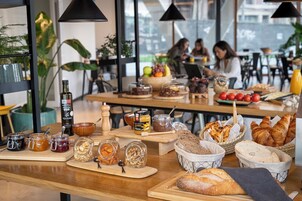 Un café que exhibe una variedad de alimentos y condimentos, incluyendo frascos de miel, mermeladas y frutos secos, además de panes y pasteles.