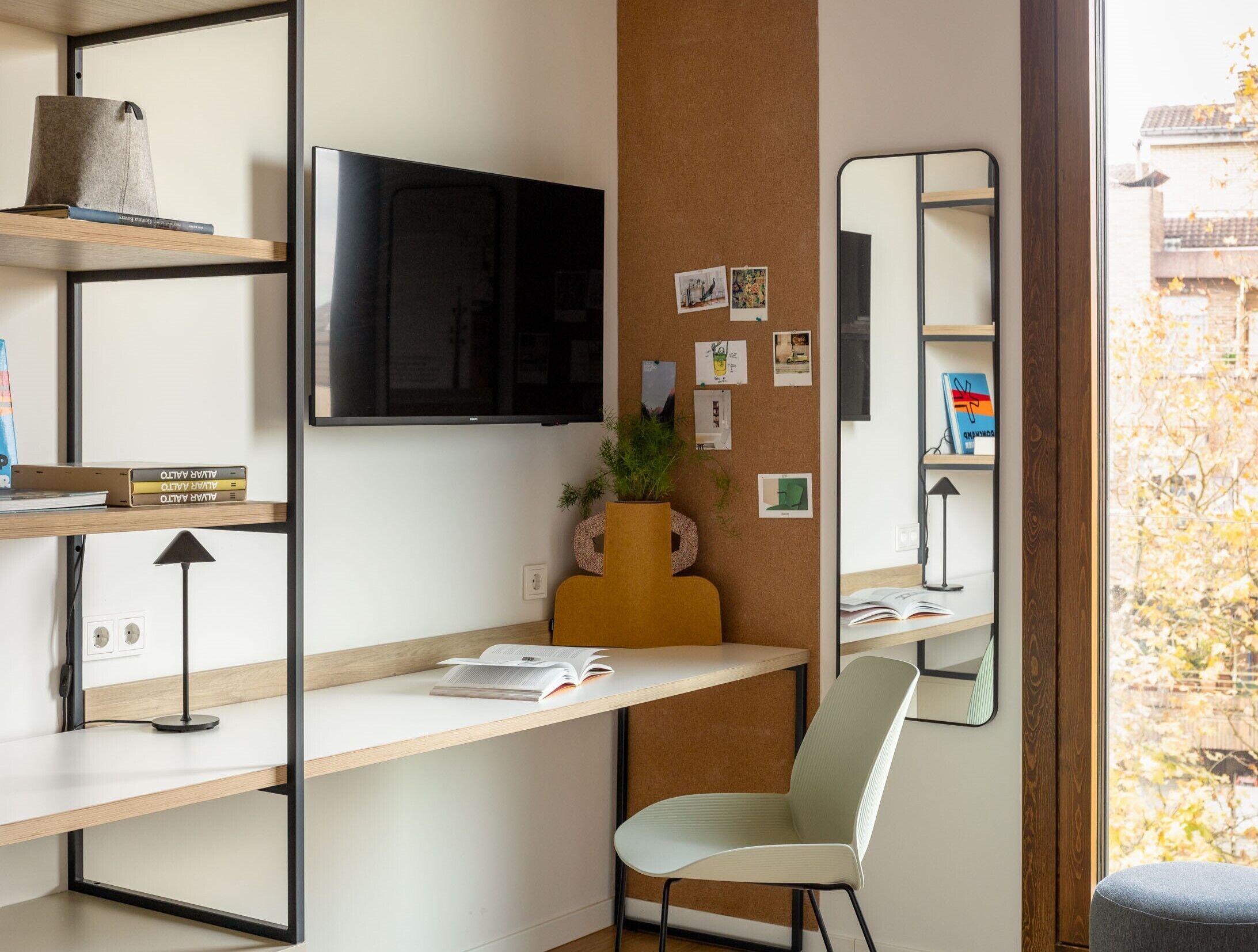 Un espacio de oficina moderno con escritorio, silla, estantería y un espejo grande.