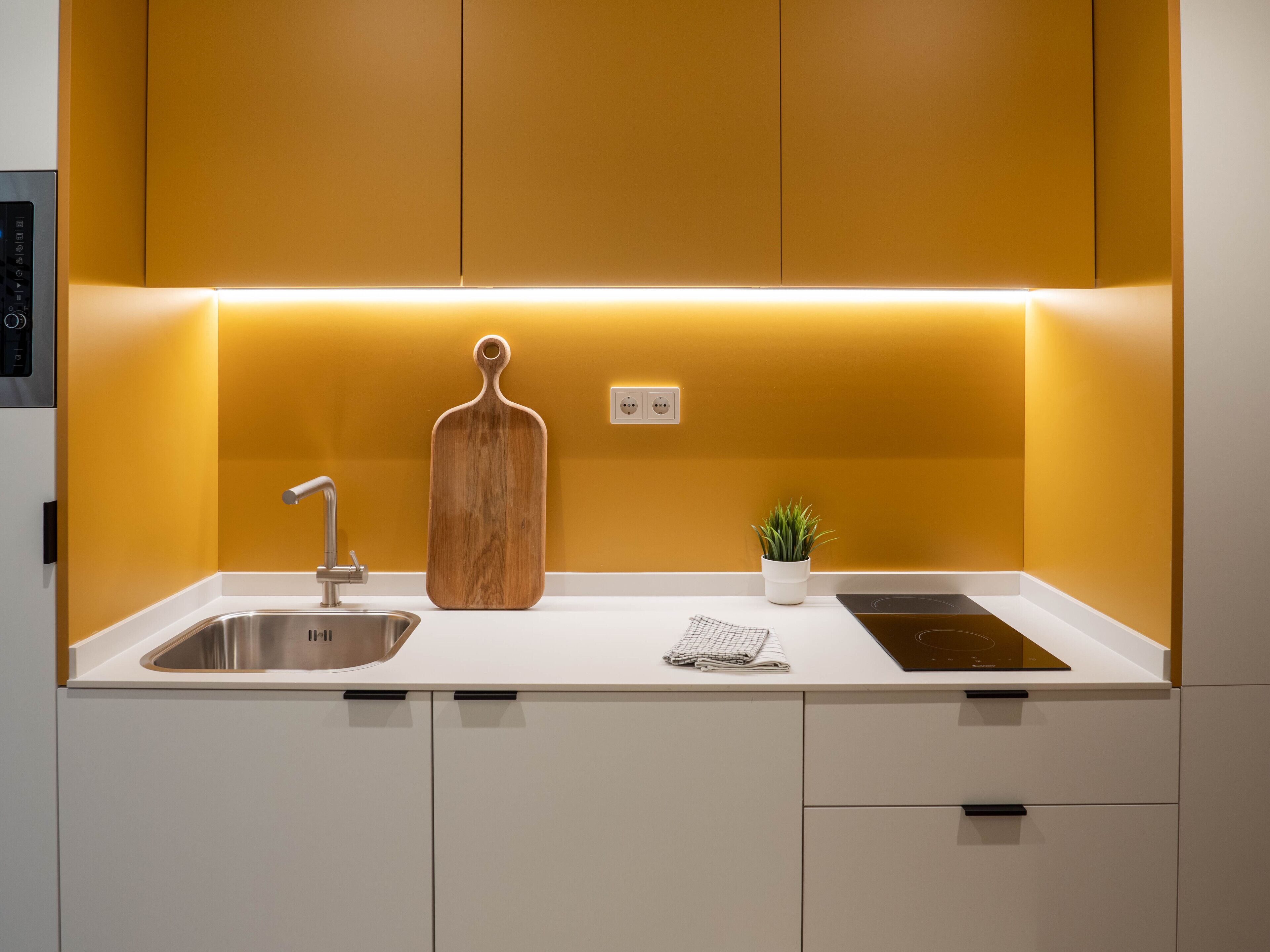 Eine moderne Küche mit weißer Arbeitsplatte, Spüle aus Edelstahl, Schneidebrett aus Holz und einem kleinen Topfpflanzen.
